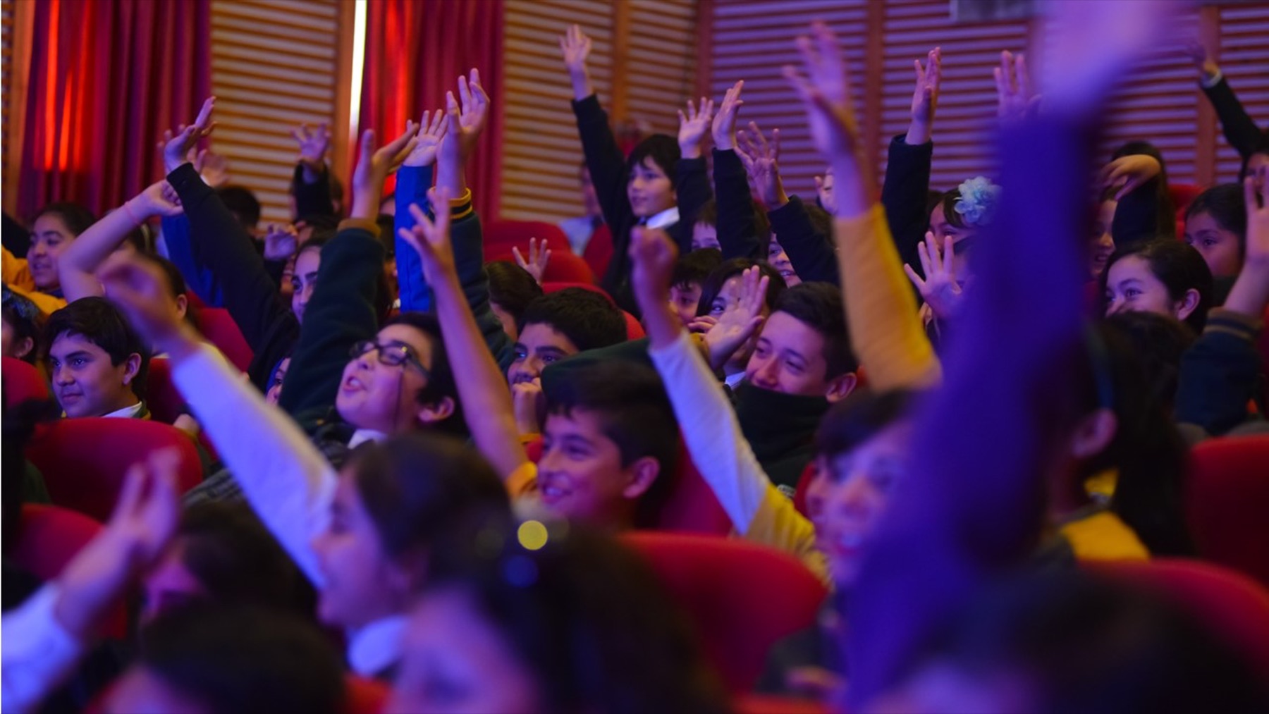 Niñas y niños levantan las manos durante una función