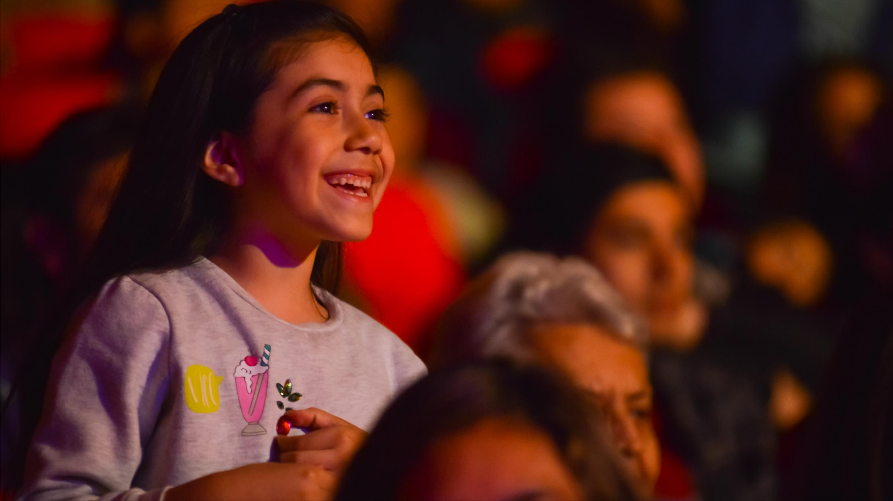 Niña sonríe entre el público durante una función de Atacamagica Kusiy